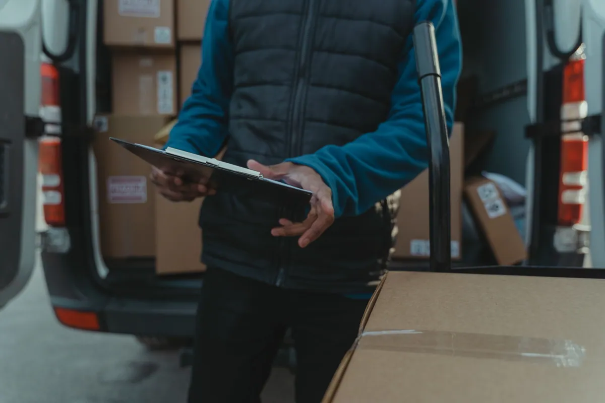 A person checking a clipboard beside packages in an open cargo van