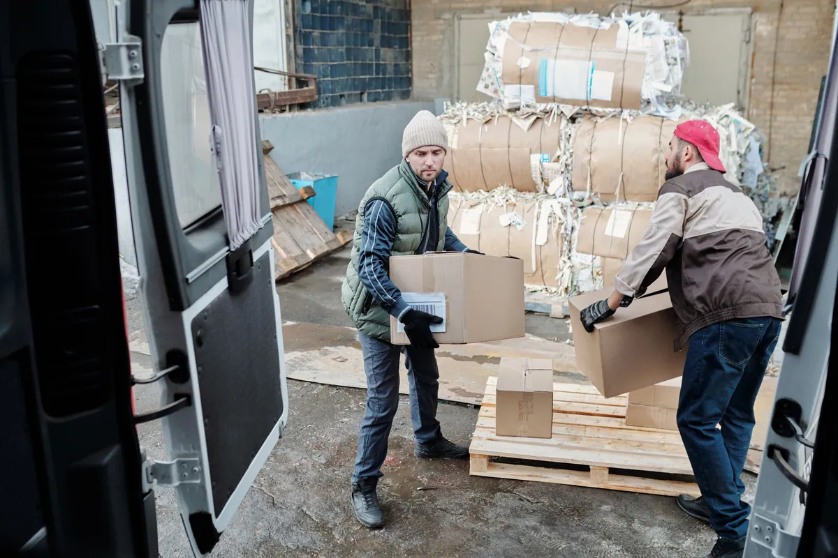 Two workers handling shipping cartons beside an open delivery van